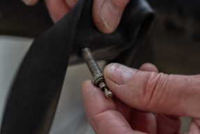 Close-up of hands holding a French valve on a bicycle inner tube during repair.