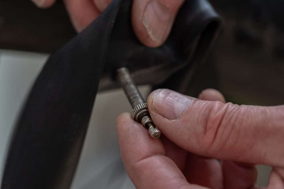 Close-up of hands holding a French valve on a bicycle inner tube during repair.
